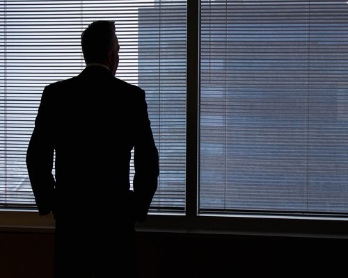 A man looking thoughtfully out of a modern office window over the city
